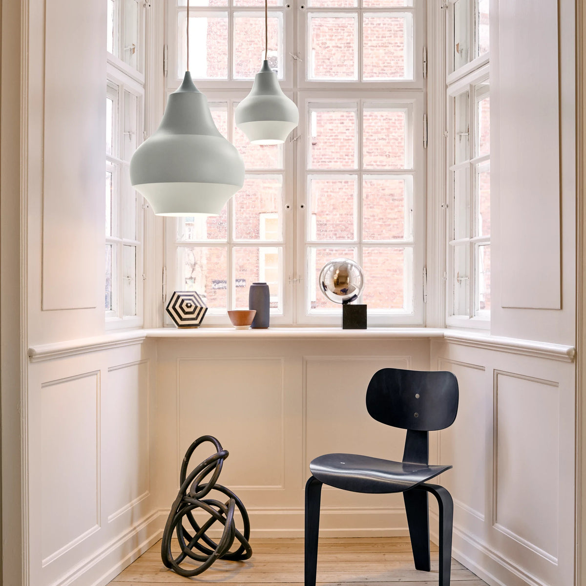 Two Cirque pendants in Grey Top hanging in a white panelled window bay above a black chair