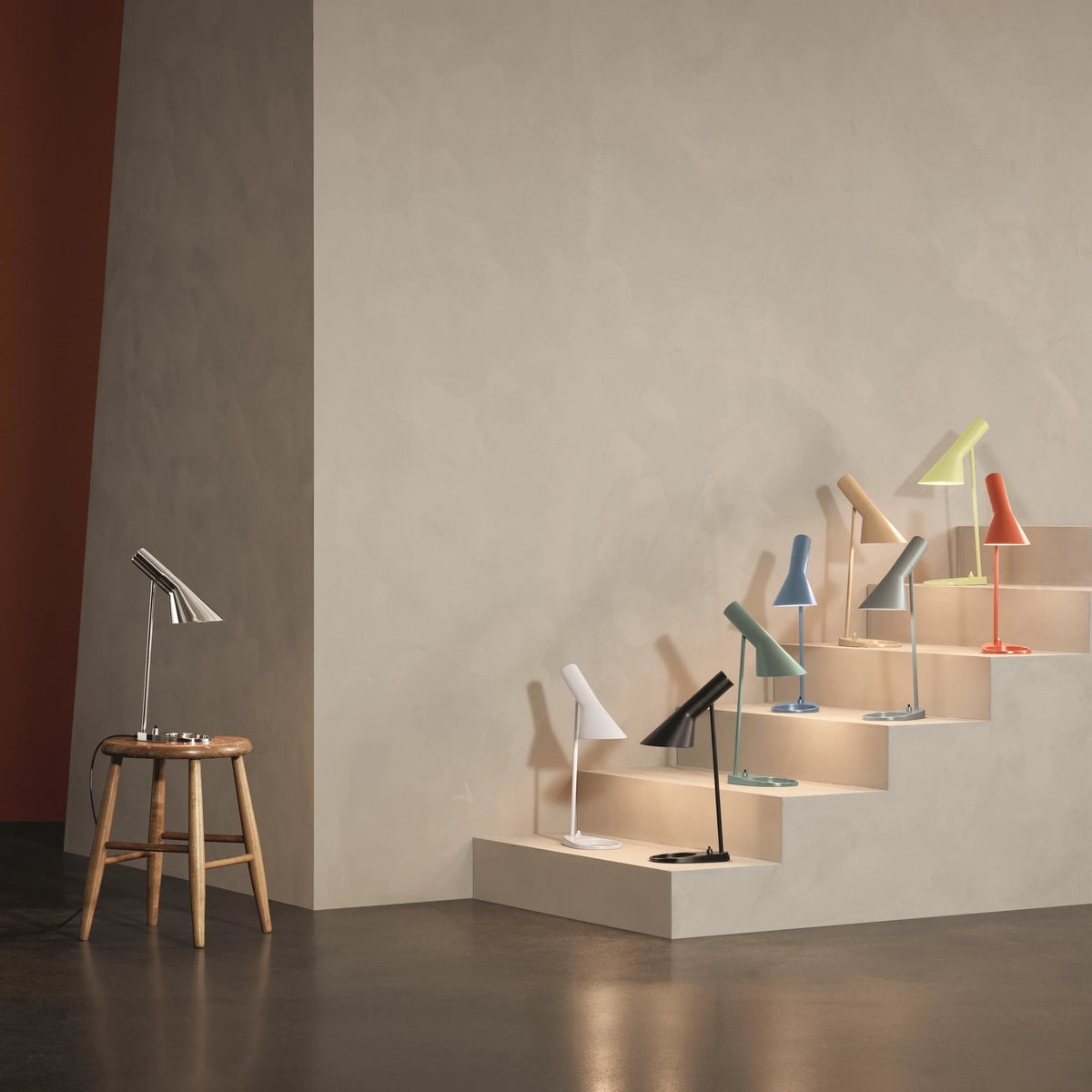 AJ table lamps in several painted colours and stainless steel arranged on steps in a pale interior