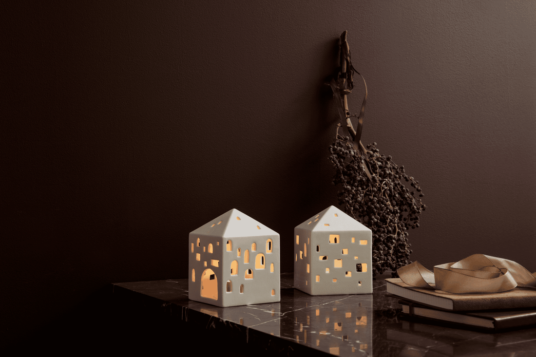 Two Kähler Urbania ceramic light houses lit with tealights on a dark marble surface