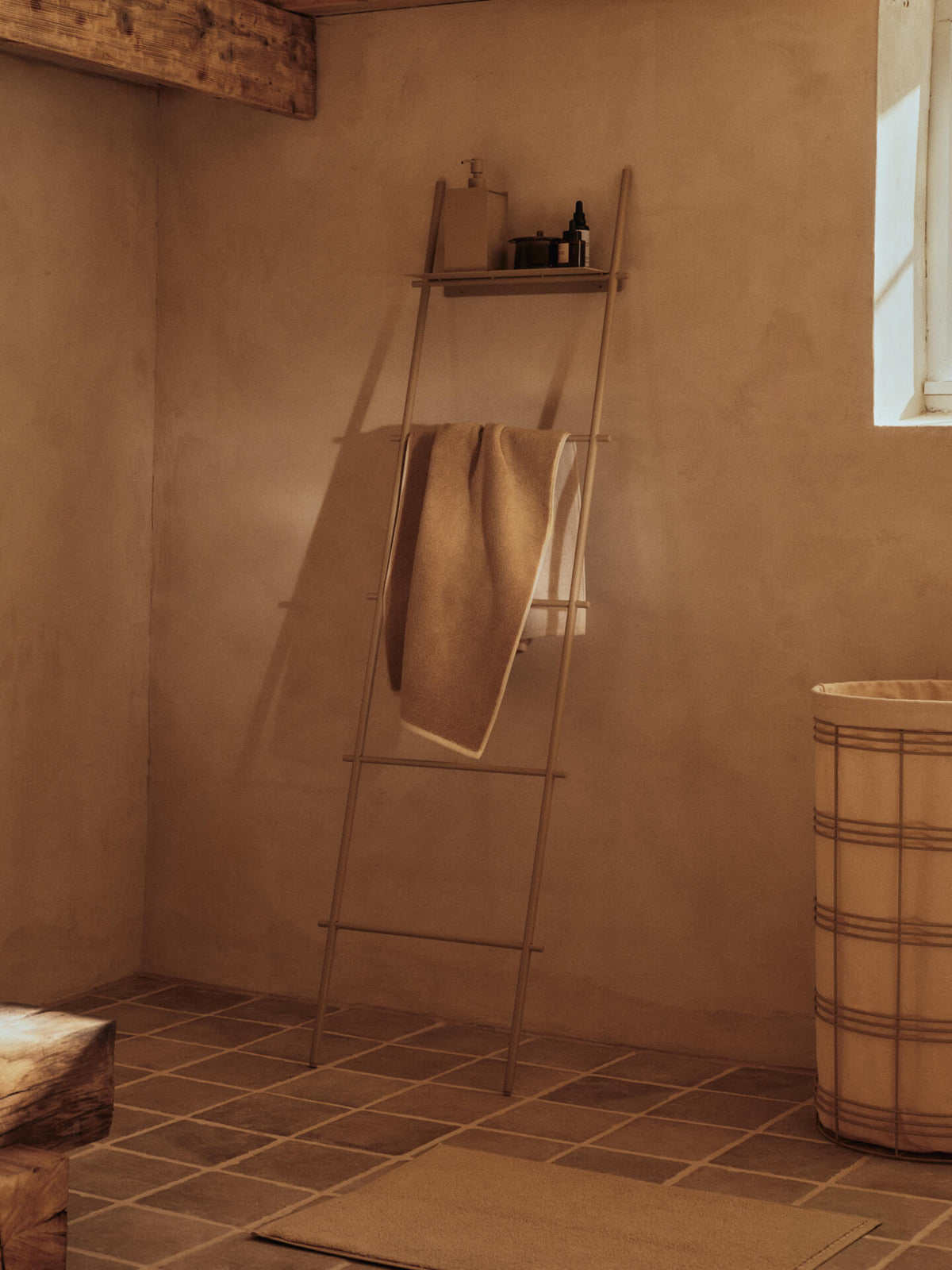 ferm LIVING Dora Towel Ladder in Cashmere leaning against a warm plaster wall in a bathroom with a towel hanging from a rung
